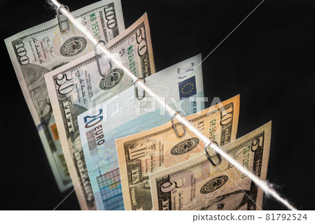 Different new dollar bills with twenty euro bill between them are hanging on the dark background. Closeup, selective focus 81792524