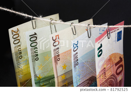 Parts of different euro bills are hanging on clerical clips on a rope on the dark background. Closeup, selective focus 81792525