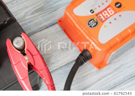 A car battery with red and black battery jumper clamps and a car battery charger. Closeup, selective focus 81792543