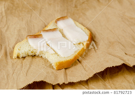 Sandwich bite on a brown background. Sandwich with salted lard. Three slices of pork fat with burnt skin and a slice of wheat bread. Brown paper bag. Sandwich bite on a brown background. Sandwich with salted lard. Three slices of pork fat with burnt skin and a slice of wheat bread. Brown paper bag. 81792723