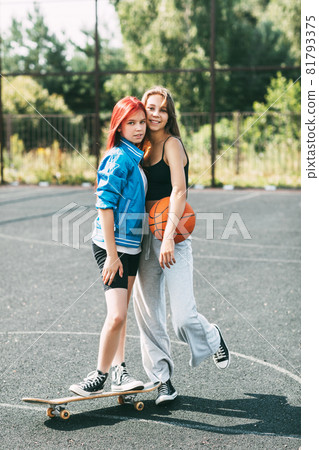 Portrait of two teenage girls with a basketball and a skateboard on a sports field Portrait of two teenage girls with a basketball and a skateboard on a sports field 81793375