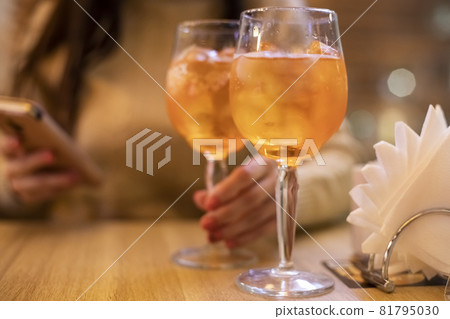 Two glasses of wine with spritz stand on a wooden table in a cafe, in the rays of the setting sun. Italian alcoholic drink with oranges and ice. Close-up, selective focus, Two glasses of wine with spritz stand on a wooden table in a cafe, in the rays of the setting sun. Italian alcoholic drink with oranges and ice. Close-up, selective focus, 81795030
