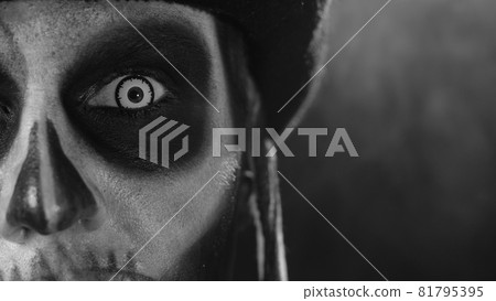 Close-up shot of face in skeleton Halloween makeup opening eyes with white pupil, trying to scare 81795395