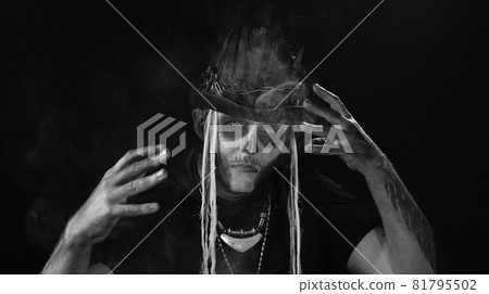 Man in skeleton Halloween cosplay costume. Guy in creepy skull makeup making faces, looks mysterious Man in skeleton Halloween cosplay costume. Guy in creepy skull makeup making faces, looks mysterious 81795502