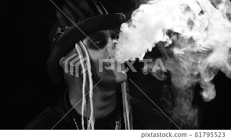 Sinister man with professional skull makeup exhaling cigarette smoke from his mouth and nose Sinister man with professional skull makeup exhaling cigarette smoke from his mouth and nose 81795523