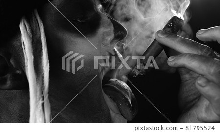 Frightening man in skeleton Halloween cosplay costume smoking cigar, making faces, showing tongue 81795524