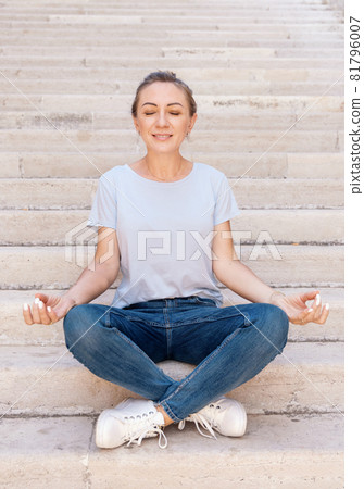 Women wearing t-shirt and jeans sitting on stairs and meditating 81796007