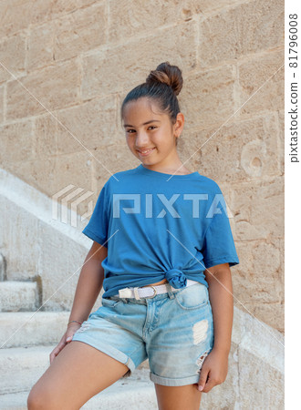 Smiling girl kid wearing t-shirt and shorts stays on stone stairs 81796008