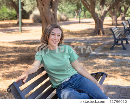 Women wearing t-shirt and jeans sits on the bench in the park 81796010