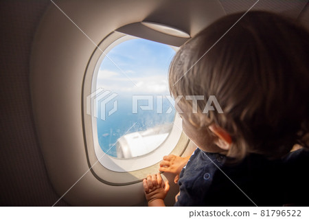 Toddler looks at the ground through the porthole of a flying plane 81796522