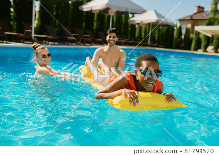 Cheerful friends swim on a mattress in the pool Cheerful friends swim on a mattress in the pool 81799520
