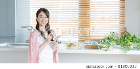 Banner size of a young woman operating a smartphone in the dining kitchen Banner size of a young woman operating a smartphone in the dining kitchen 81800038