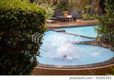 splash of water after jumping into a tropical outdoor pool in the pouring rain 81800163