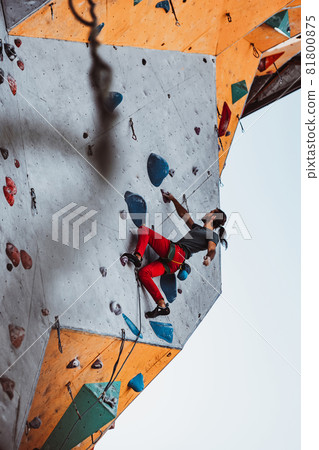 Hard level. Young man professional rock climber practicing at training center in sunny day, outdoors. Concept of healthy lifestyle, tourism, nature, motion. Hard level. Young man professional rock climber practicing at training center in sunny day, outdoors. Concept of healthy lifestyle, tourism, nature, motion. 81800875