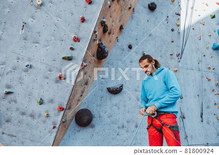 Safety climbing. Young man professional rock climber checking sports equipment before climbing at training center in sunny day, outdoors. Safety climbing. Young man professional rock climber checking sports equipment before climbing at training center in sunny day, outdoors. 81800924