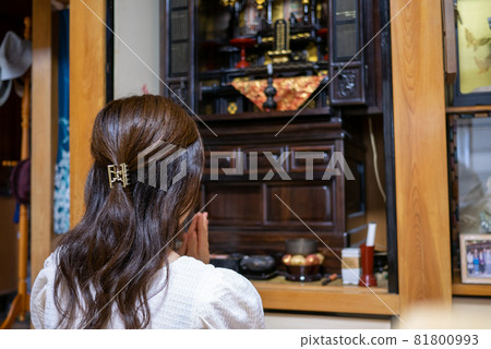 Rear view of a young woman holding hands on a Buddhist altar between Buddhas 81800993