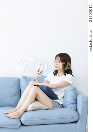 A woman using a smartphone while relaxing on the sofa 81803013
