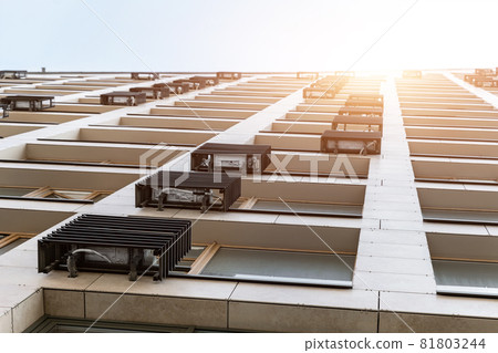 Bottom pov of new modern residential apartment office building facade with many air conditioners mounted covered by metal casing against sky and sun light. Condo exterior wall with ac outdoor units 81803244
