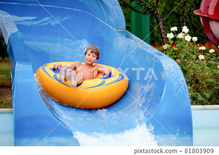 happy an 8 year old boy is riding in the water Park on inflatable circles on water slides with splash happy an 8 year old boy is riding in the water Park on inflatable circles on water slides with splash 81803909