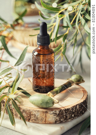 Amber glass transparent bottle with Jade face roller and eucalyptus leaves. Skin Care Anti-Aging concept, face massage Amber glass transparent bottle with Jade face roller and eucalyptus leaves. Skin Care Anti-Aging concept, face massage 81804891