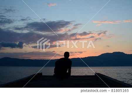 一個男人在碼頭上凝視著蒼白的日落的剪影 81805165