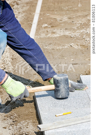 A worker places granite tiles on the sidewalk, leveling them with a rubber mallet. Vertical image. 81806113