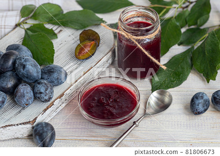 Plum jam in a jar. In the background there are plums. Tkemali sauce. Preparing for winter. Light background. Plum jam in a jar. In the background there are plums. Tkemali sauce. Preparing for winter. Light background. 81806673