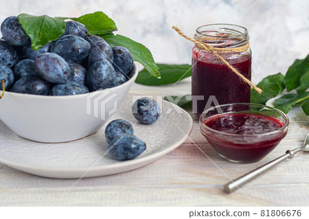 Plum jam in a jar. In the background there are plums. Tkemali sauce. Preparing for winter. Light background. Plum jam in a jar. In the background there are plums. Tkemali sauce. Preparing for winter. Light background. 81806676