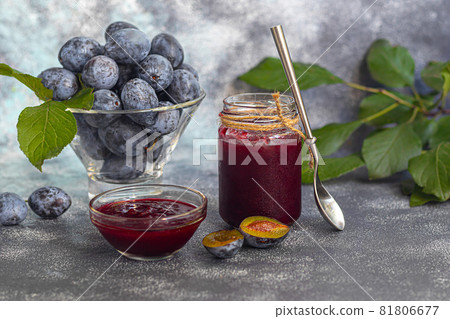 Plum jam in a jar. In the background there are plums. Tkemali sauce. Preparing for winter. Light background. Plum jam in a jar. In the background there are plums. Tkemali sauce. Preparing for winter. Light background. 81806677