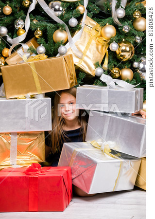 Happy preteen girl sitting among wrapped presents beside decorated Christmas tree on boxing day Happy preteen girl sitting among wrapped presents beside decorated Christmas tree on boxing day 81808428
