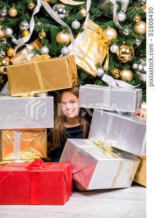 Happy preteen girl sitting among wrapped presents beside decorated Christmas tree on boxing day Happy preteen girl sitting among wrapped presents beside decorated Christmas tree on boxing day 81808430