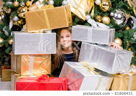 Happy preteen girl sitting among wrapped presents beside decorated Christmas tree on boxing day Happy preteen girl sitting among wrapped presents beside decorated Christmas tree on boxing day 81808431