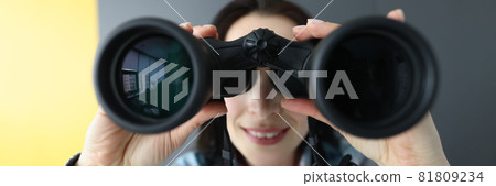 Woman looking through black binoculars and holding it with her hands Woman looking through black binoculars and holding it with her hands 81809234