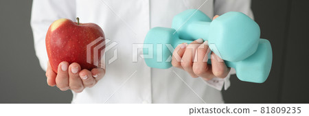 Doctor holding dumbbells and red apple closeup 81809235