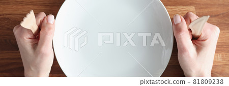 Female hands holding wooden fork and knife near white plate closeup Female hands holding wooden fork and knife near white plate closeup 81809238