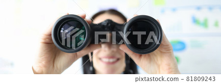 Woman looking through black binoculars in office closeup Woman looking through black binoculars in office closeup 81809243