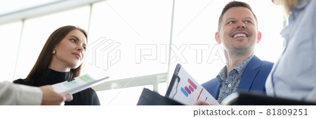 Smiling man and women sitting at meeting with documents in hands Smiling man and women sitting at meeting with documents in hands 81809251