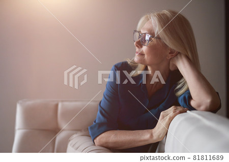 Calm mature woman in eyewear relaxing on a couch at home in the living room 81811689
