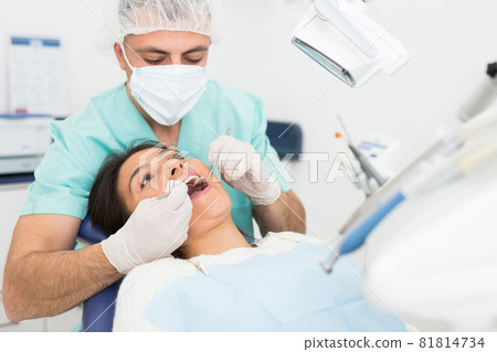 Dentist man examining a latin female patient teeth 81814734