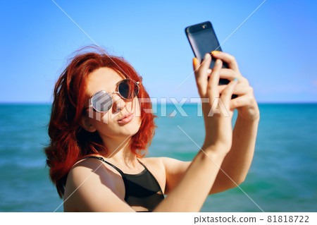 Red-haired woman takes selfie on smartphone camera. Red-haired woman takes selfie on smartphone camera. 81818722