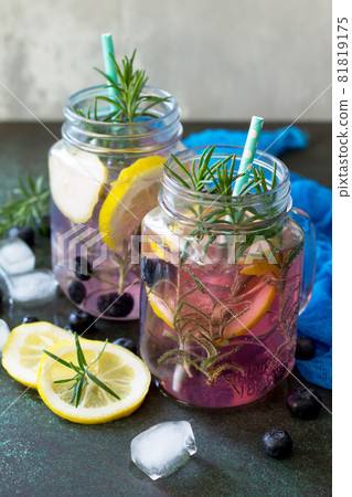 Lemonade or cocktail with blueberries and rosemary, cold refreshing drink with ice on dark concrete or stone table. Lemonade or cocktail with blueberries and rosemary, cold refreshing drink with ice on dark concrete or stone table. 81819175