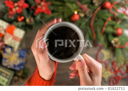 A woman holds a hot new year's coffee. Christmas decorations, gifts and wooden background.  81822711
