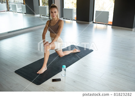 Portrait of young sportive happy girl, coach in sportswear doing yoga on sports mat at meditation center, indoors. Concept of healthy lifestyle Portrait of young sportive happy girl, coach in sportswear doing yoga on sports mat at meditation center, indoors. Concept of healthy lifestyle 81823282