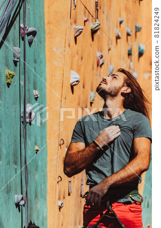 Portrait of Caucasian man professional rock climber standing at front of climbing wall at training center in sunny day, outdoors. Concept of healthy lifestyle, sport, motion. Portrait of Caucasian man professional rock climber standing at front of climbing wall at training center in sunny day, outdoors. Concept of healthy lifestyle, sport, motion. 81824249