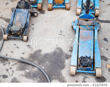 few old hydraulic jacks for replacement of tires on outdoor ground of car repair shop 81825656