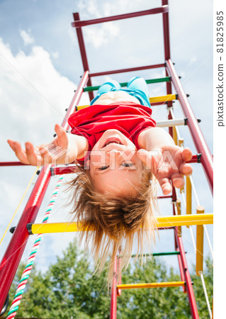 Happy little girl hanging from a jungle gym in a summer garden 81825985