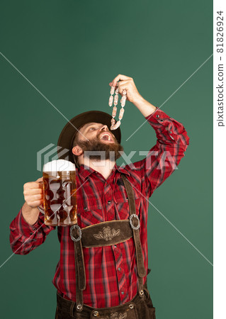 Portrait of bearded man in traditional Bavarian costume with sausages having fun isolated over green background. Oktoberfest, festival, traditions concept 81826924