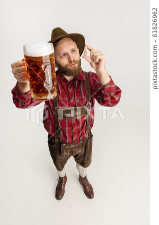 Comic portrait of bearded man in hat and traditional Bavarian costume holding huge mug, glass of light frothy beer and isolated over white background. Oktoberfest 81826962