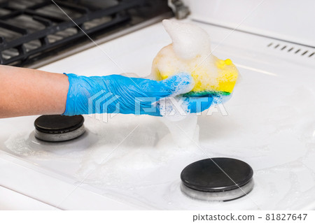 Woman's hand in a household glove washing sponge with foam a dirty gas stove background, close up Woman's hand in a household glove washing sponge with foam a dirty gas stove background, close up 81827647