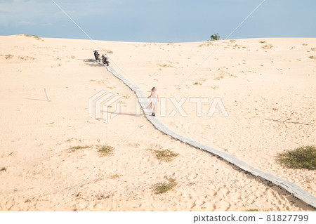 Picturesque view of beautiful blond woman in long casual dress walking in desert with white sand on sunny day during summer vacation. Sand dunes. Picturesque view of beautiful blond woman in long casual dress walking in desert with white sand on sunny day during summer vacation. Sand dunes. 81827799